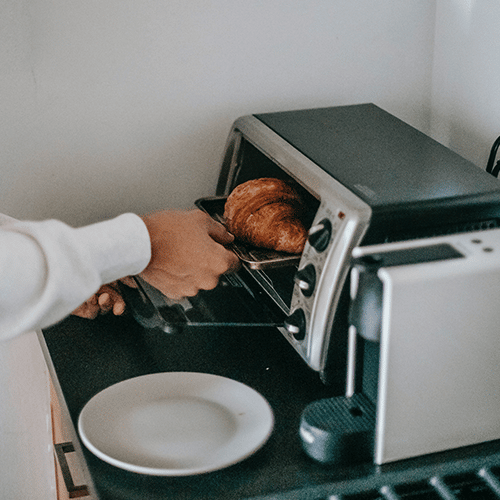 person getting a croissant out of a small toaster oven